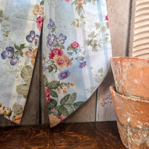 A decorative vintage fabric bow handmade with a padded form and long tapering tails, finished with an antiqued brass ring for hanging. This Country House Bow features a striped floral fabric in soft pastel tones, perfect for interior styling, doors, mantels, and weddings.