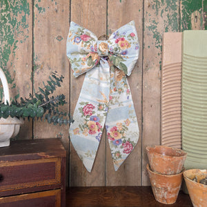 A handmade vintage fabric bow from the Jennings & Cox Country House collection, crafted in limited numbers with a padded structure and long tapering tails. This large floral stripe bow is finished with a brass hanging ring, ideal for doors, mantels, and decorative styling.