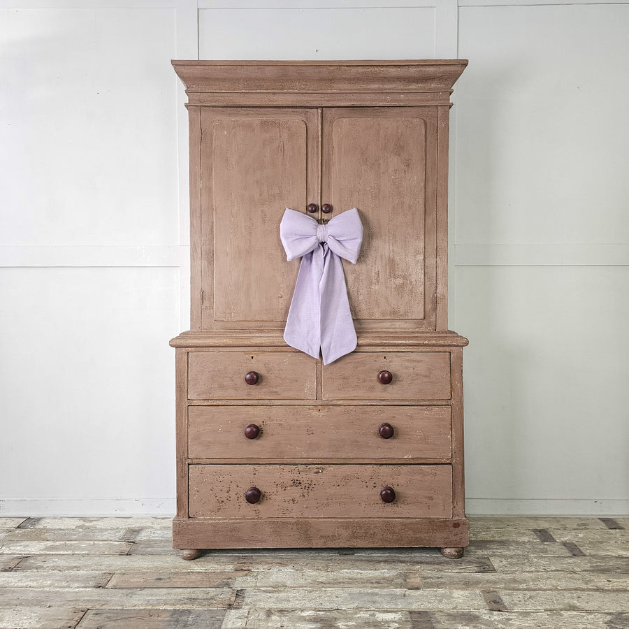 Dusky pink painted pine cupboard with two doors and four drawers.
