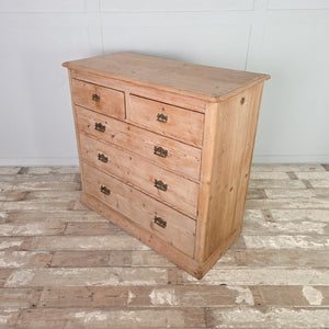 An antique Victorian pine chest of drawers with five drawers arranged in a two-over-three configuration. The stripped pine finish and brass handles suit this farmhouse style storage chest for use in a bedroom or placed in a hallway.