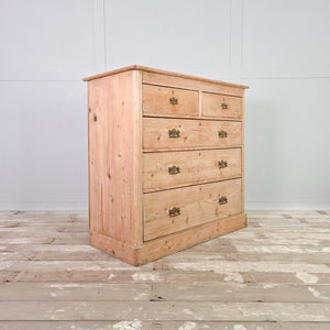 A 19th century pine chest of drawers with five drawers arranged in a two-over-three layout. Finished in stripped pine, this farmhouse style chest works well as bedroom storage or as a sideboard in a living space.