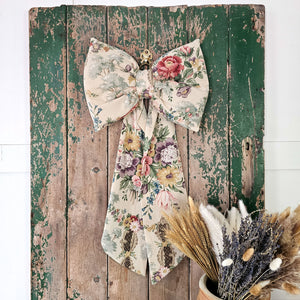 Country house style floral bow with vibrant flowers on a cream background.