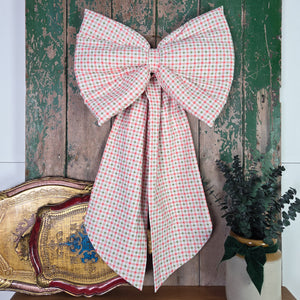 A handmade vintage fabric bow featuring a Laura Ashley gingham pattern in green, red and white. The padded structure, shaped tails and brass hanging hoop create a simple cottage style decorative piece for the home.