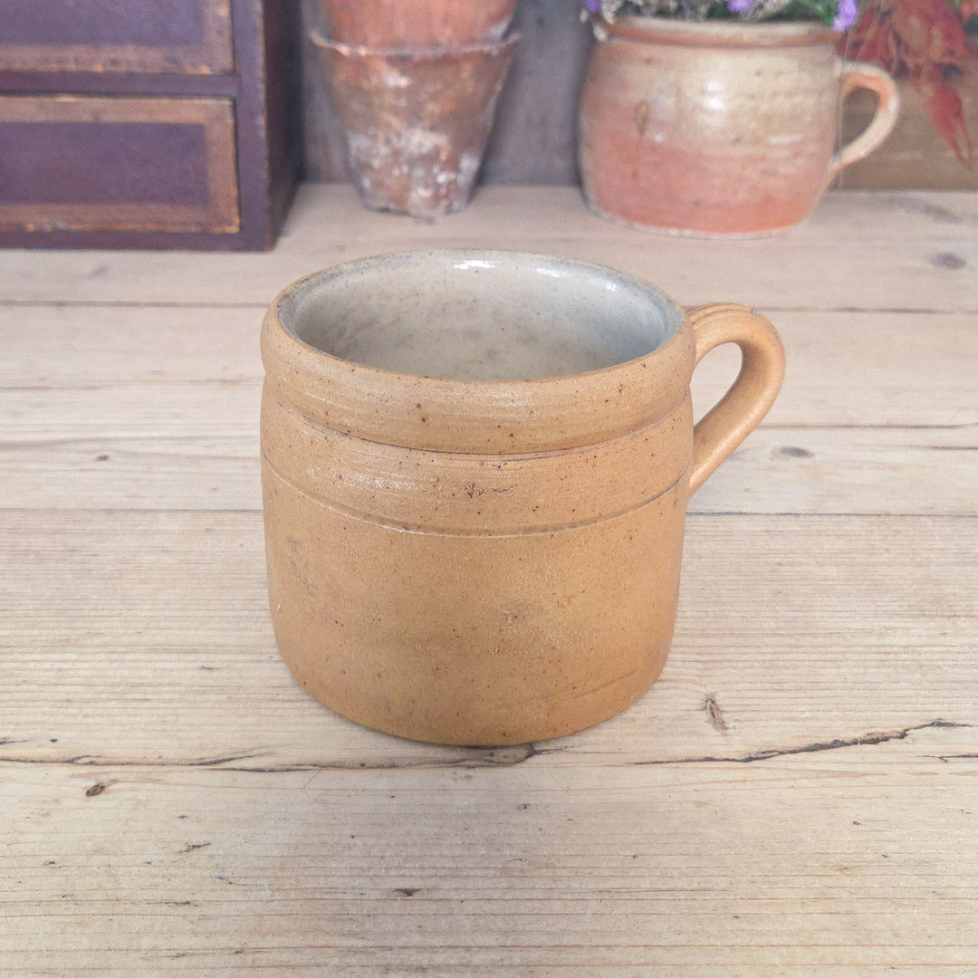 Rustic French stoneware pot with a distinctive handle and lightly glazed surface. Sometimes described as a rillette or confit jar, this vintage French pot reflects classic utilitarian design. It’s practical for holding utensils, storing kitchen tools, or displaying small plants, combining everyday function with traditional craftsmanship.