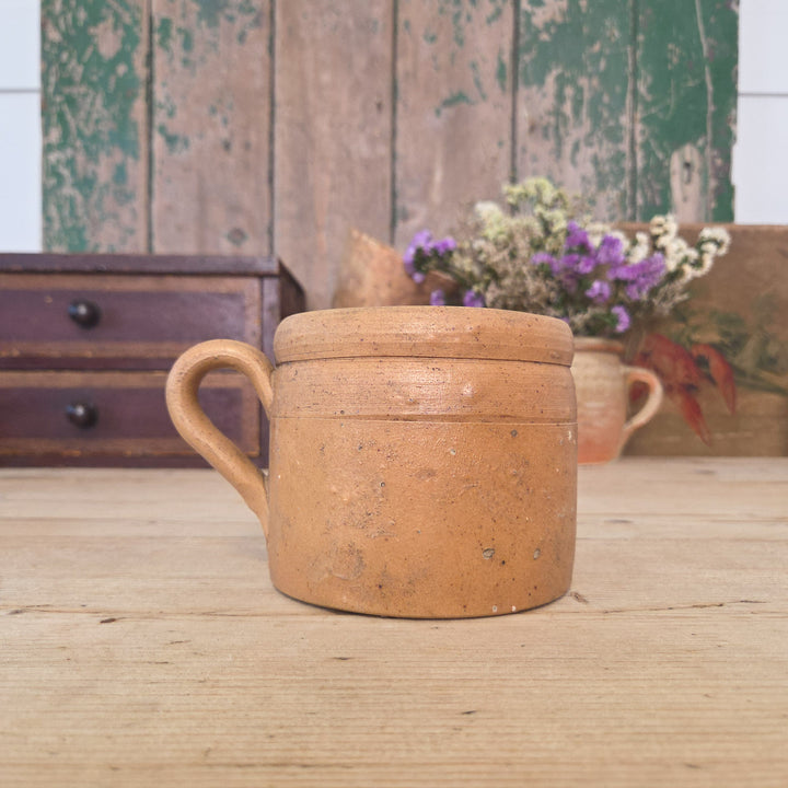 A vintage French stoneware pot with rounded body, single handle and glazed finish in warm earthy tones. Sometimes known as a confit or rillette pot, it’s a traditional French kitchen jar now used for utensil storage or displaying herbs and small plants.