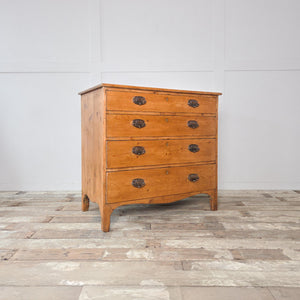 Antique pine chest of drawers from the Georgian period, showing a four drawer layout with decorative brass plate drop handles and a shaped apron to the base.
