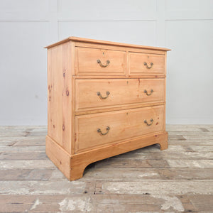 An early 20th century antique pine chest of drawers with four drawers arranged in a two-over-two layout, finished with brass swan-neck swing handles and raised on a plinth base with decorative cut-out. Ideal for storing clothing or linens in the bedroom, or for use in a hallway or landing.