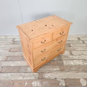 A four drawer antique pine chest of drawers from the early 20th century, fitted with brass swan-neck swing handles and standing on a plinth base with a decorative cut-out to the front. A practical option for bedroom storage, or for use in a hallway or landing to store everyday household items.