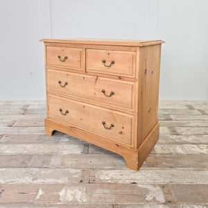 This antique pine chest of drawers dates from the early 20th century and features four drawers in a two-over-two arrangement, brass swan-neck swing handles and a plinth base with shaped cut-out detail. Suitable for use in the bedroom for clothing and linens, or in a hallway or landing for storage.