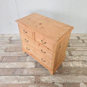An early 20th century four drawer antique pine chest of drawers, with a two-over-two layout, brass swan-neck swing handles and a plinth base finished with a decorative cut-out. A versatile storage piece that works well in the bedroom or placed in a hallway or landing.