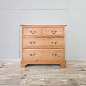 An antique pine chest of drawers from the early 20th century, with four drawers arranged in a two-over-two layout, brass swan-neck swing handles and a plinth base with shaped cut-out detail. A practical storage piece for use in the bedroom or in a hallway or landing.
