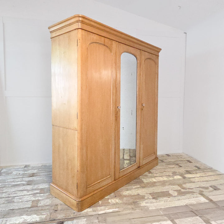 Antique pine triple wardrobe from the Victorian period with mirrored centre door, brass fittings, and solid pine construction. The wardrobe features hanging rails, drawers, and a lift-up compartment, offering practical 19th century bedroom storage in authentic antique pine.