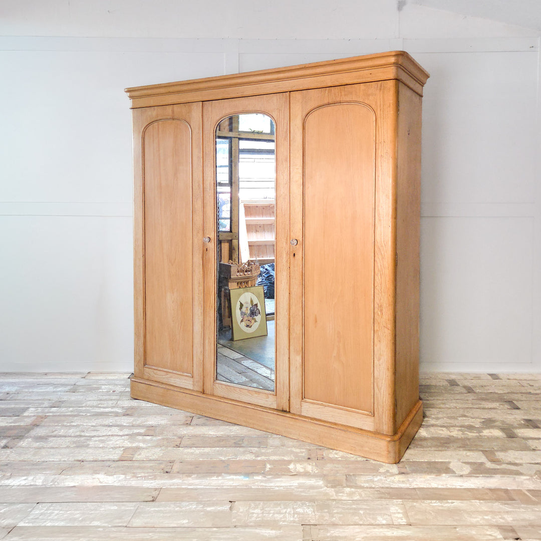 Antique Victorian pine wardrobe with three doors and a mirrored centre panel, dating to the late 19th century. This large triple wardrobe includes drawers, hanging space, and a hidden compartment, demonstrating the quality craftsmanship of Victorian pine bedroom furniture.