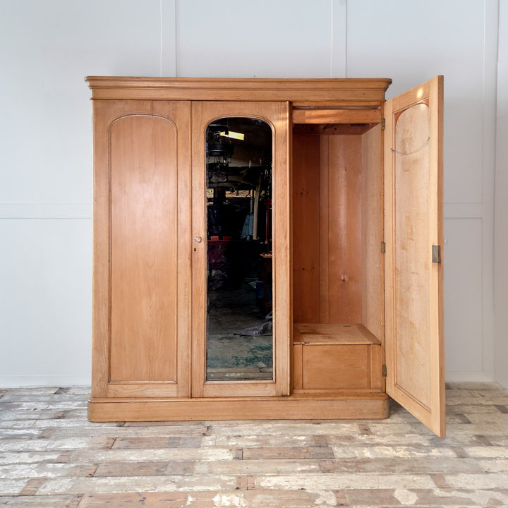 Antique Victorian triple wardrobe made from pine with a central mirrored door flanked by two outer doors. Inside, the left section has drawers and a hanging rail, while the right section includes a slide-out tray, hanging rail, and concealed compartment. A 19th century pine wardrobe showcasing the craftsmanship and functional storage typical of Victorian furniture.