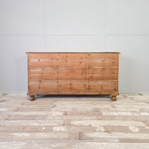 An antique Victorian pine dresser base dating from the 19th century, featuring an open shelving section at the centre with seven drawers arranged to either side. Raised on bun feet with a moulded top edge, it works well as a sideboard in a living space or as storage in a hallway.