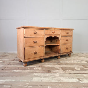 A 19th century Victorian pine dresser base with seven graduated drawers and central open shelves. Original turned wooden knobs are fitted throughout, and the piece can be used as a kitchen dresser base or placed along a wall in a living room.