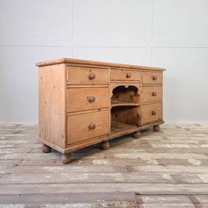 A rustic Victorian pine dresser base with open shelving at the centre and seven drawers arranged either side. The graduated drawers and shelving make it a practical option for kitchen storage or for use as a sideboard in a living space.