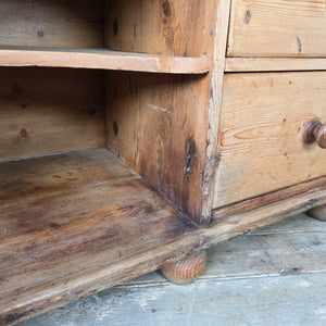 A farmhouse-style Victorian pine dresser base dating from the 19th century, featuring seven graduated drawers and a central open shelving section. Raised on bun feet with a moulded top, it can be used in a kitchen or placed in a hallway for additional storage.