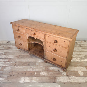 A 19th century pine dresser base from the Victorian era, constructed with open shelves at the centre and seven drawers arranged either side. The graduated drawers make it suitable for use in a kitchen or along a wall in a hallway.