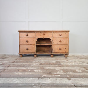 A farmhouse-style Victorian pine dresser base dating from the 19th century, featuring seven graduated drawers and central open shelving. The piece works well in a kitchen for everyday storage or in a hallway for household items.