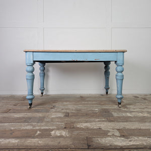 A 19th century Victorian pine farmhouse table featuring a scrubbed natural pine top and a powder blue painted base. The table stands on turned legs, includes a small front drawer, and is raised on castors, making it suitable for use as a dining table.

