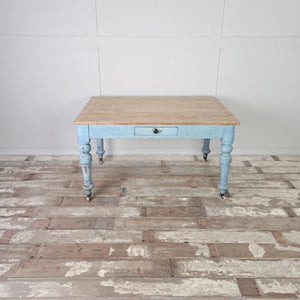 An antique pine farmhouse table from the Victorian period with a scrubbed natural pine top and a painted base in a soft powder blue shade. Raised on turned legs with a single drawer, it is a flexible piece suitable for kitchen, dining, or desk use.