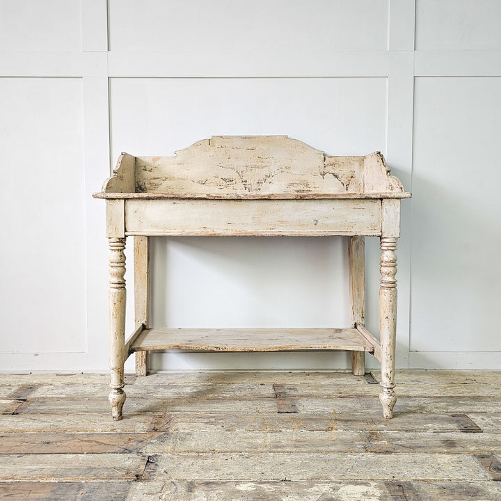Antique English pine washstand with distressed white finish, featuring Victorian-style shaping and turned legs.