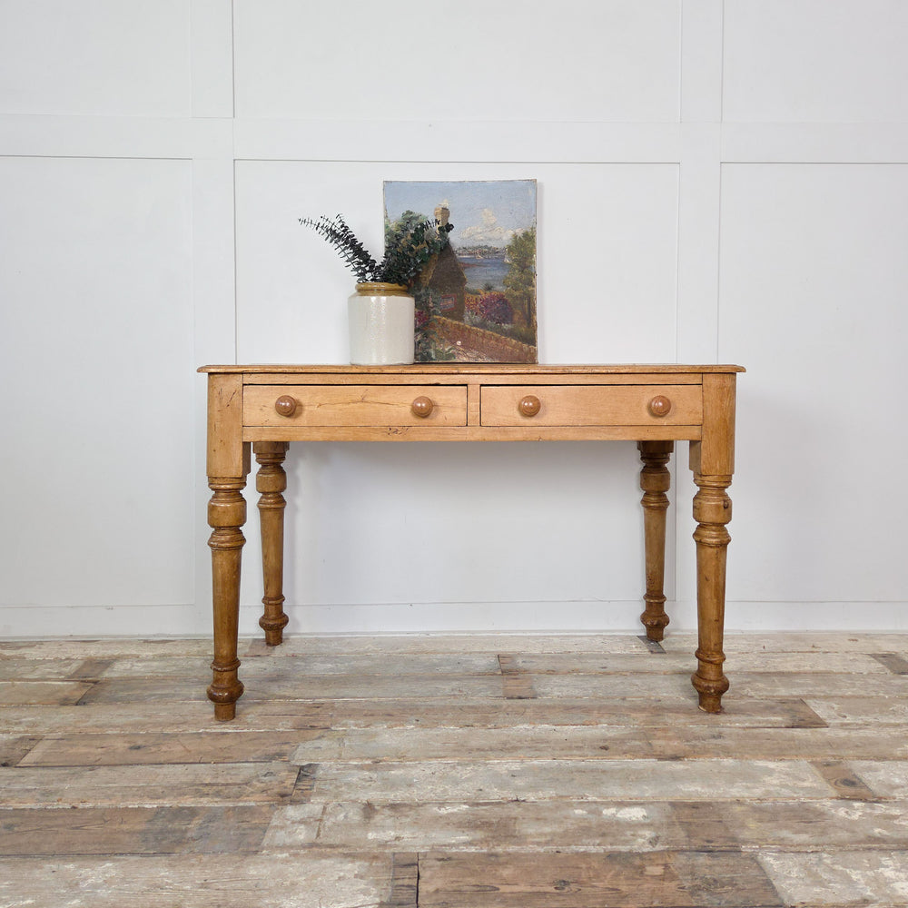 A 19th-century antique pine console table or desk with two drawers and turned legs, finished in wax to enrich the wood’s tone. A versatile farmhouse-style piece for hallway or study.