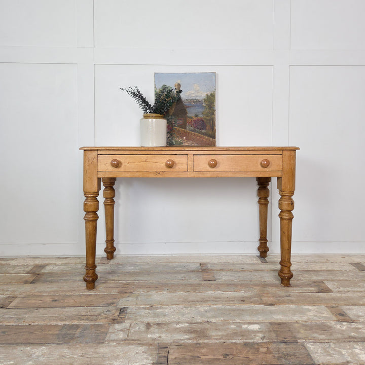 A 19th-century antique pine console table or desk with two drawers and turned legs, finished in wax to enrich the wood’s tone. A versatile farmhouse-style piece for hallway or study.