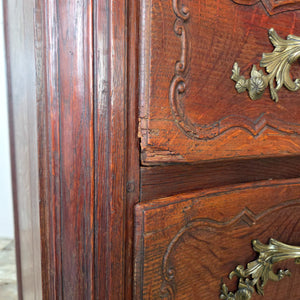 An antique French walnut serpentine chest of drawers from the 19th century. The piece has four full-width drawers with carved fronts, ornate brass handles, and escutcheons, all raised on short carved legs with a warm walnut patina developed through age.