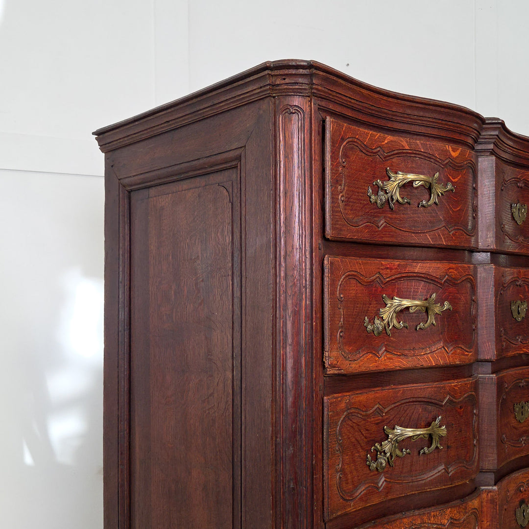 19th century French walnut serpentine chest of drawers. This antique commode includes four full-width drawers with carved fronts, ornate brass fittings, and short carved legs. The walnut surface shows the depth and tone of natural patina.