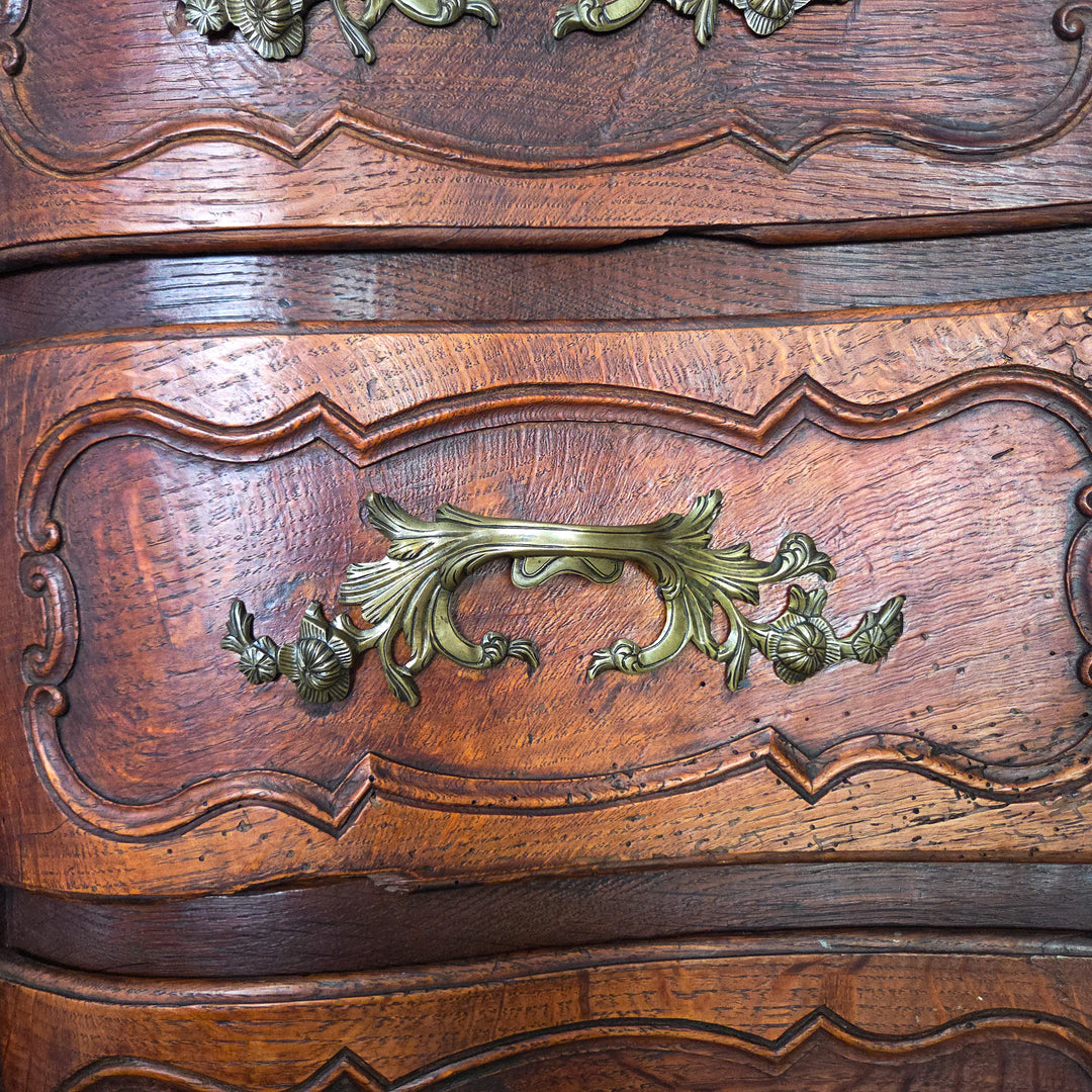 A 19th century French walnut serpentine chest of drawers with four carved drawers, ornate brass handles, and escutcheons. The walnut surface has aged to a warm patina, and the chest stands on short carved legs, maintaining its strong form.