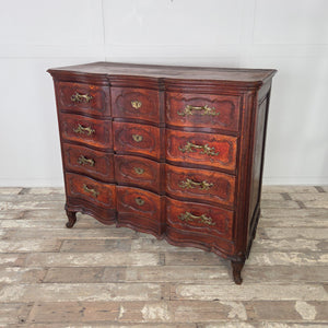 Antique French walnut chest of drawers in serpentine form from the 19th century. Features four deep drawers with carved fronts, ornate brass handles, and escutcheons, all supported on short carved legs with an aged walnut finish.