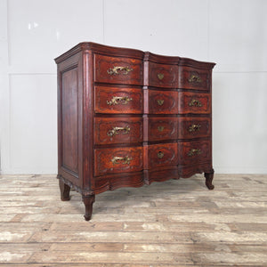 An antique French walnut serpentine chest of drawers from the 19th century. Features four full-width drawers with carved fronts, ornate brass handles and matching escutcheons. Raised on short carved feet, the chest displays a naturally aged walnut patina.