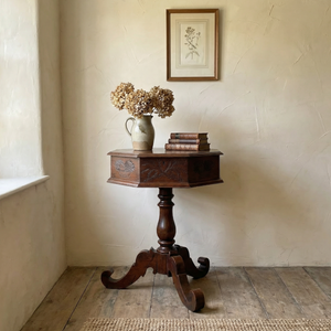 Antique Victorian oak sewing table with octagonal hinged lid and decorative carved motifs on tripod base
