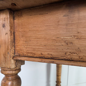 A small antique pine farmhouse table with a two-plank top and rounded edges, raised on turned legs extended at the bottom with additional timber. Featuring a simple apron, this cottage-style pine table serves well in hallways or as a small kitchen table.