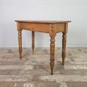 A small antique pine farmhouse table with a two-plank top, gently rounded edges and a straightforward apron. Set on decorative turned legs extended with newer timber, this country-style pine table offers a functional work surface suited to hallways or small kitchens.