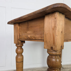 A 19th-century small antique pine table featuring a two-plank farmhouse-style top with rounded edges, supported by turned legs extended at the bottom using newer timber. With its simple apron, this pine table provides practical use in hallways or as a small kitchen table.