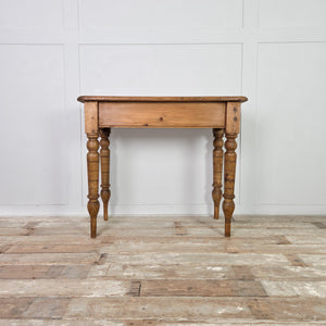 A small antique pine farmhouse table featuring a two-plank rectangular top with rounded edges, supported by turned legs extended at the base. Finished with a simple apron, this pine table provides functional country-style use in hallways or small kitchens.