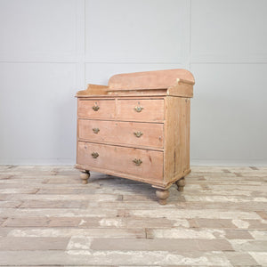 A rustic Victorian pine chest of drawers with four drawers in a two-over-two formation. The drawers are fitted with decorative brass handles, and the chest features a shaped gallery back and turned tulip bun feet.