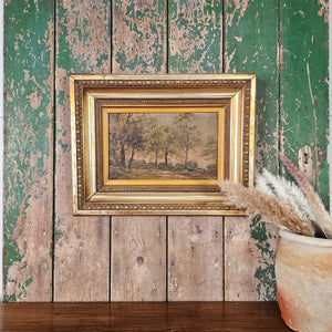 Victorian oil painting in ornate gilt frame, original 19th century artwork depicting a quiet countryside scene with trees, painted on board using soft muted colours, antique wall art for home display.

