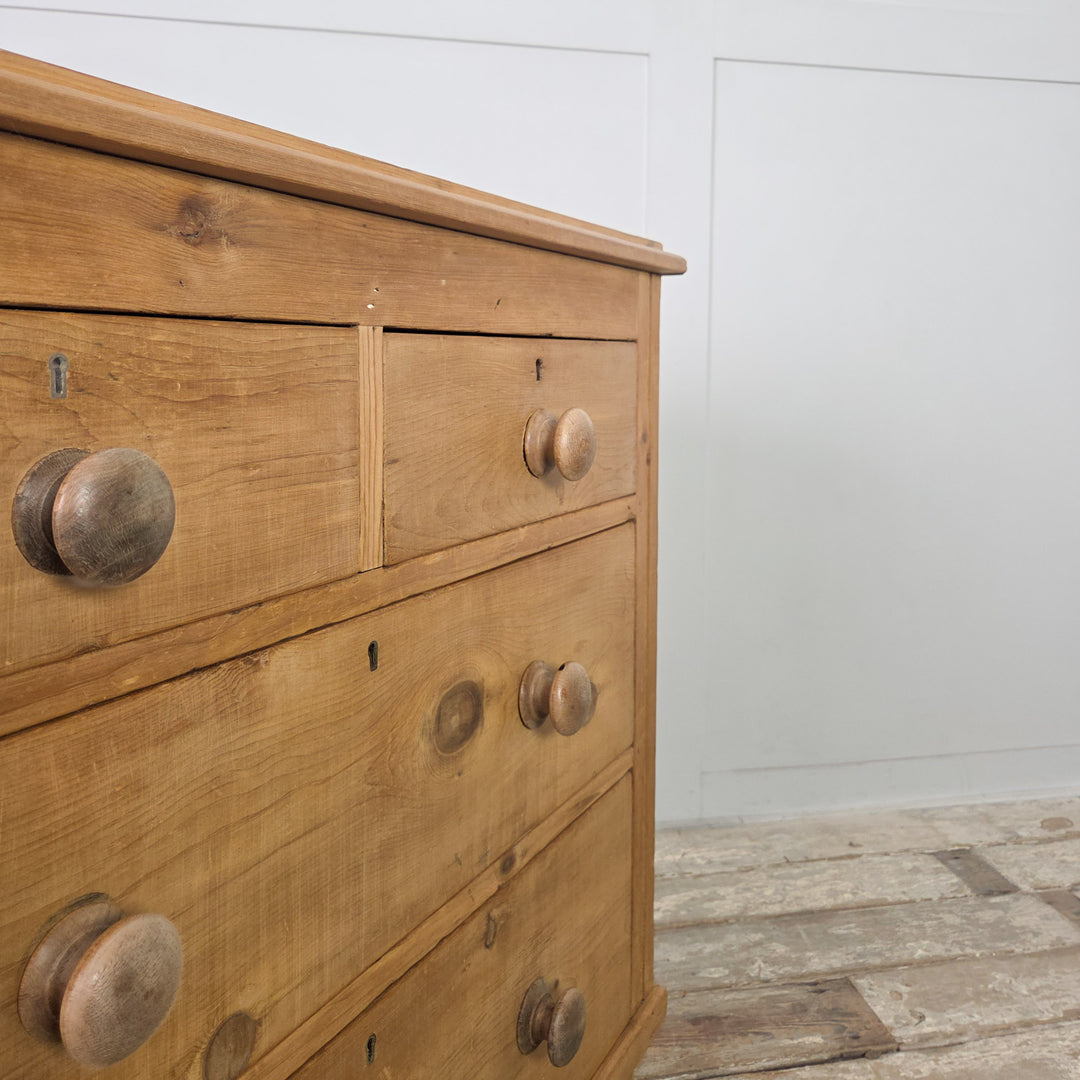 An antique Victorian pine chest with original wooden knobs, bun feet and a simple upstand to the top, providing four drawers of practical storage and displaying the natural warmth of aged pine.