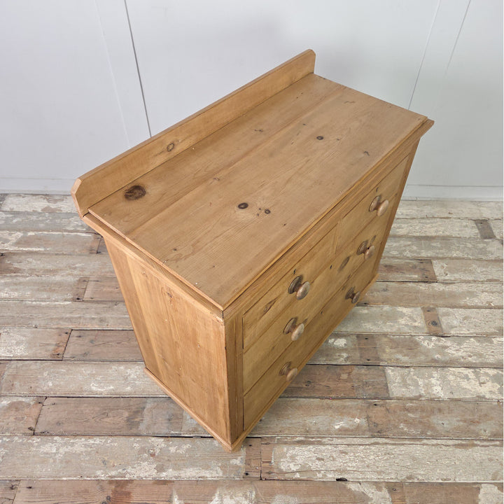 An antique pine Victorian chest of drawers with original knobs and bun feet, offering four well-sized drawers and a warm waxed surface that highlights the grain and natural patina of the pine.