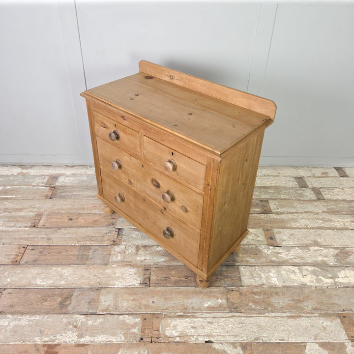A Victorian pine chest of drawers with a two-over-two configuration, standing on bun feet and finished in clear wax to retain its natural character, perfect for use as an antique dresser or sideboard.