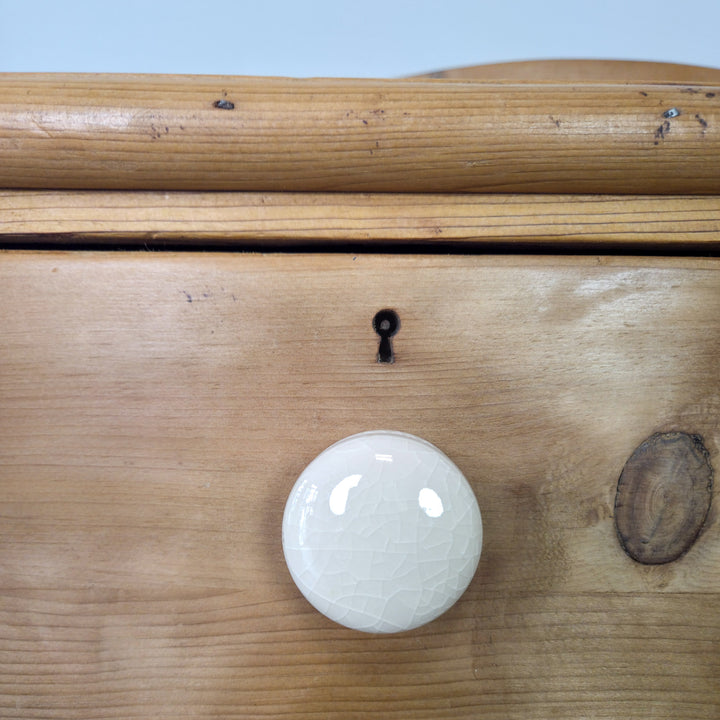 A Victorian pine chest with ceramic knobs and bun feet, offering period detail and ample drawer storage in a compact design