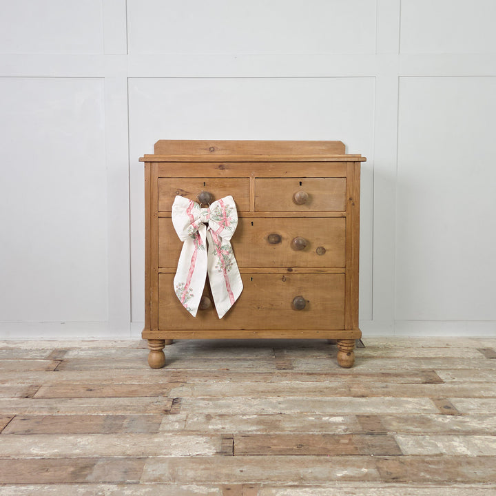 An antique Victorian pine chest with a warm wax finish, four drawers and turned bun feet, combining traditional craftsmanship with useful storage for clothes or household linens.