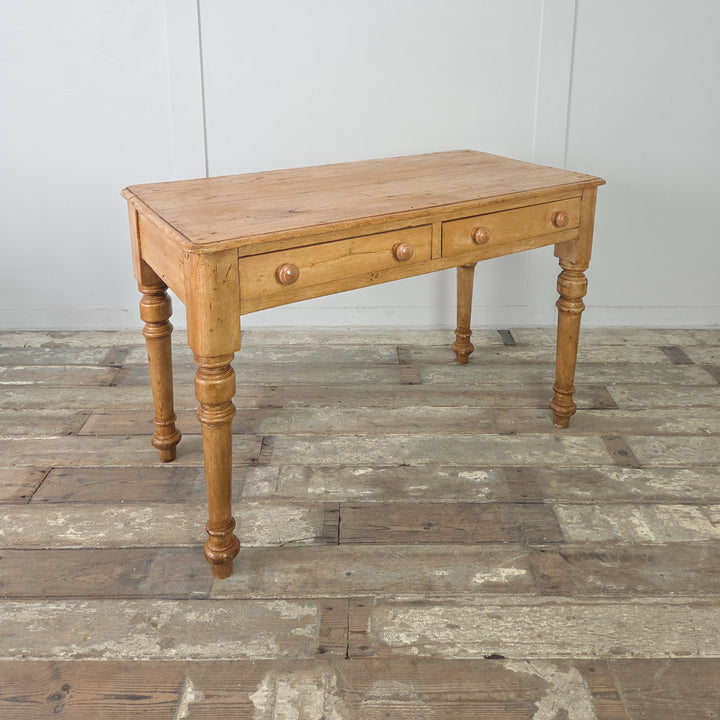 A rustic farmhouse pine console table or desk from the 19th century, raised on turned legs with a waxed pine surface, offering storage via two drawers fitted with simple wooden knobs.

