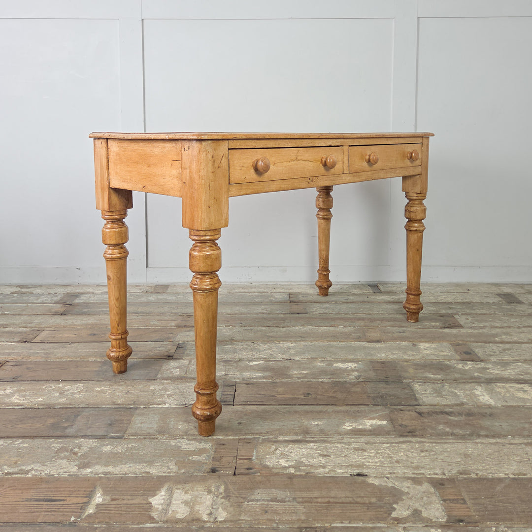 An antique pine writing desk or console table with a naturally aged finish, turned legs, and practical proportions. The table includes two drawers, each with a wooden knob, set within a plain apron.

