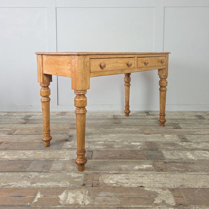 An antique pine writing desk or console table with a naturally aged finish, turned legs, and practical proportions. The table includes two drawers, each with a wooden knob, set within a plain apron.

