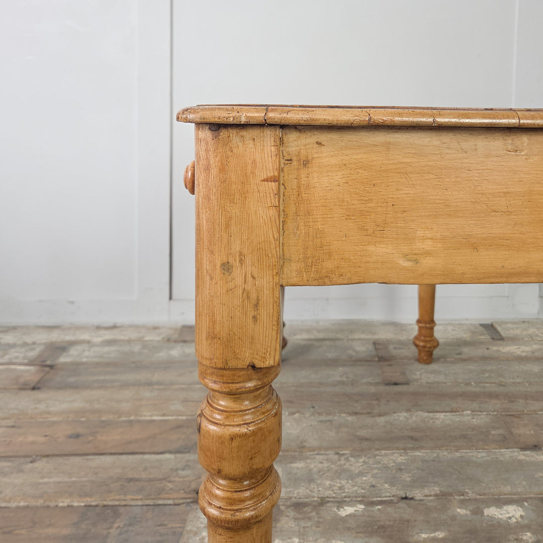 An antique 19th century pine table with two drawers and turned legs, suitable for use as a small rustic desk or hall console table. The top has been waxed to protect its worn, rich pine patina.


